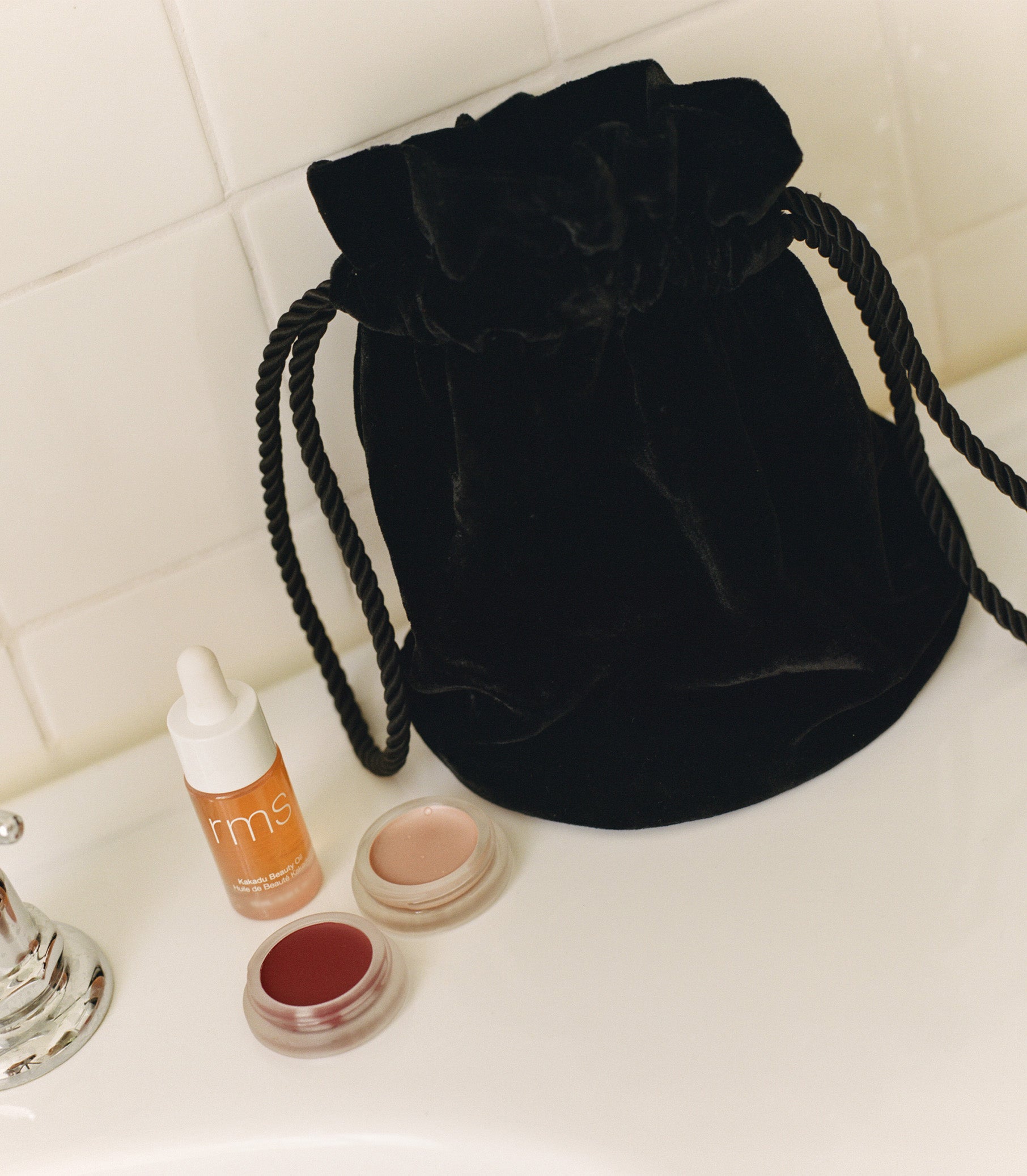 A black velvet pochette on a counter next to a lip stain, cheek luminizer, and skincare oil. 1
