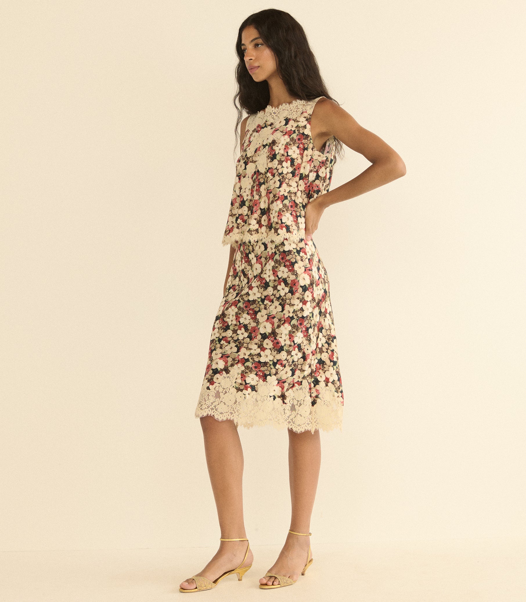 A woman models a matching set featuring a sleeveless top with a dense floral print in cream, pink, and green, finished with a cream lace hem, set against a solid cream background. 1
