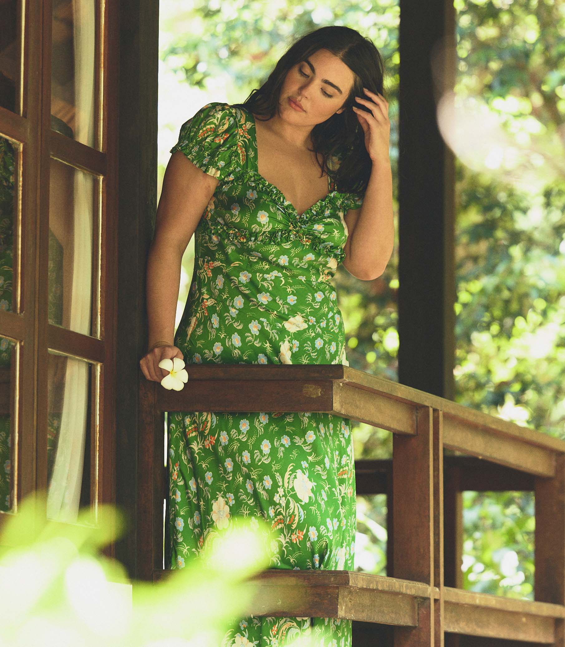 Woman in a green floral dress standing on a wooden deck with greenery in the background 1
