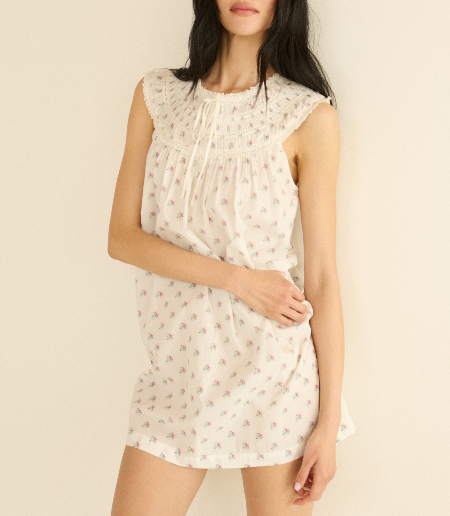 Woman wearing a white sleeveless dress with a subtle floral pattern on a plain background