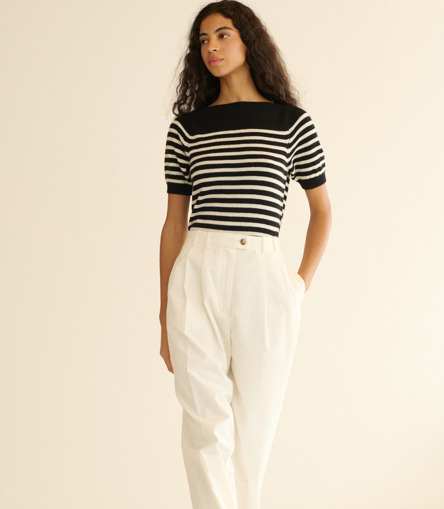 Woman wearing a black and white striped shirt with white pants on a beige background
