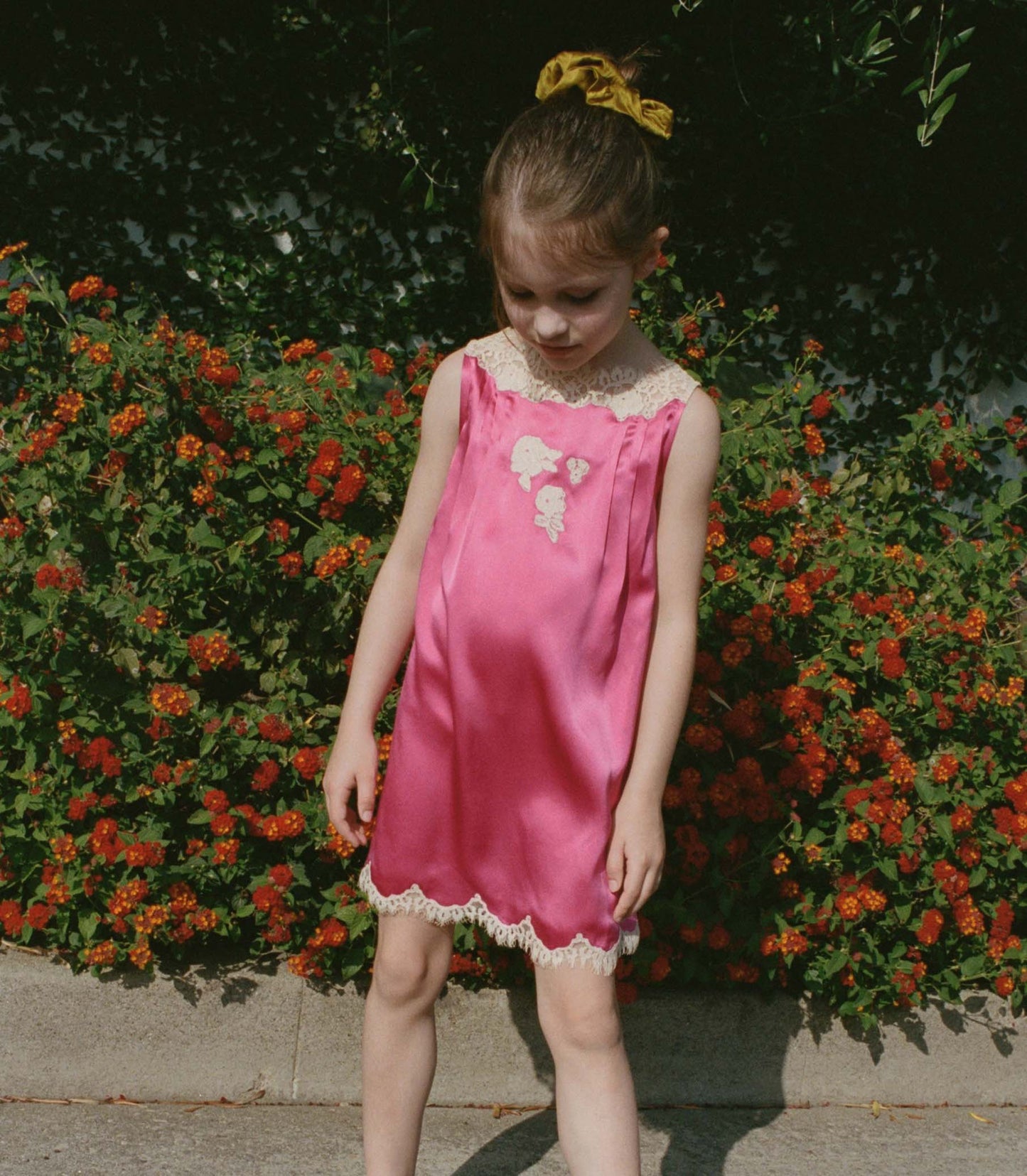Young girl in a magneta dress standing in front of flowering bushes