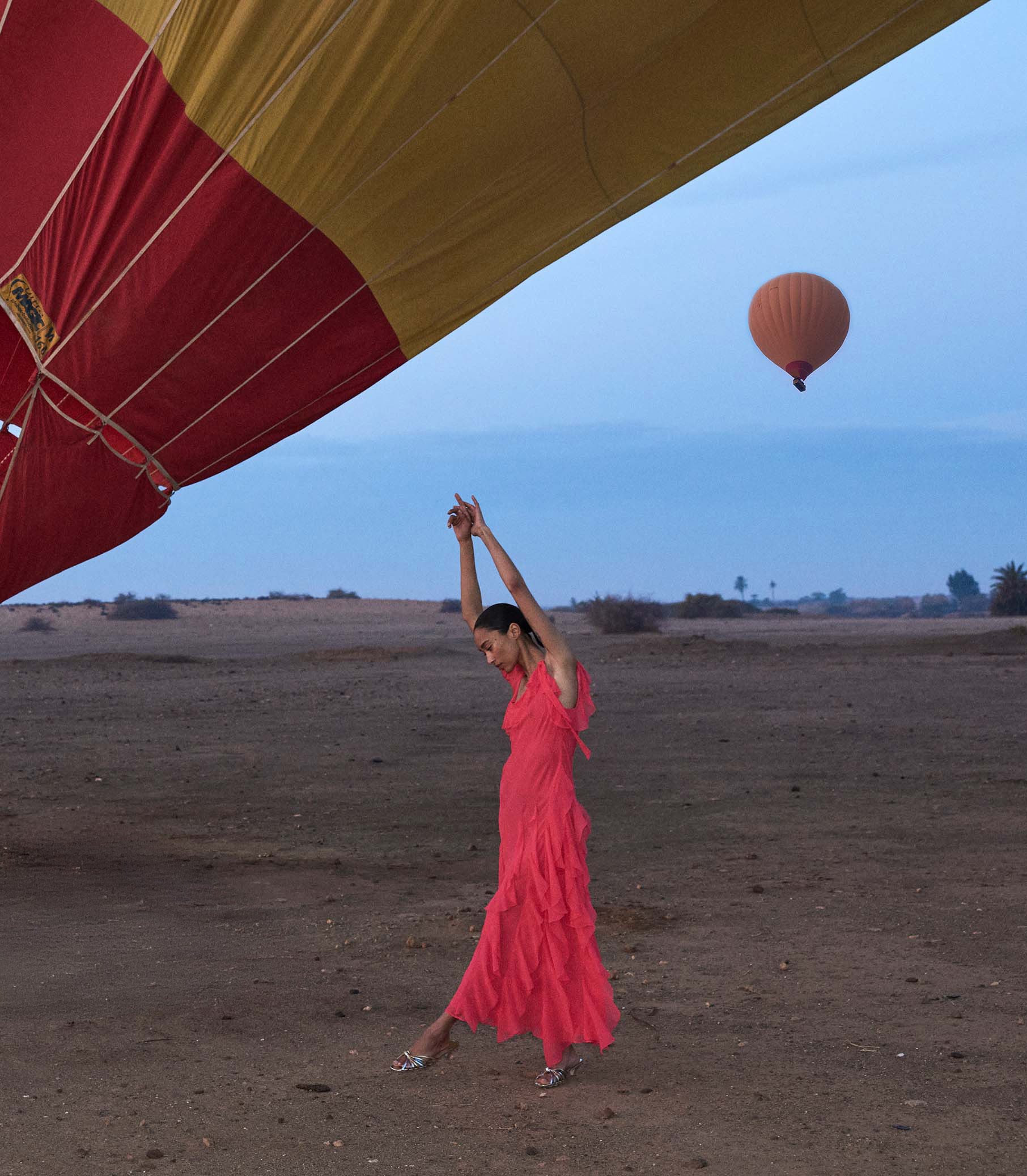 Woman in a pink dress standing on a desert with a hot air balloon in the background 1
